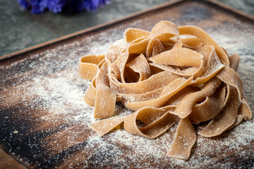Uncooked brown pasta tagliatelle with chestnuts on a wooden Board with flour