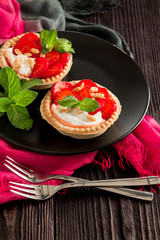 Shortbread cake with strawberries and mascarpone cream decorated with mint leaves on a brown wooden background