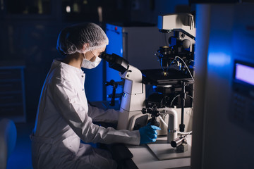 In a Modern Laboratory Scientist Conduct Experiments. Chief Research Scientist Adjusts Specimen in a Petri Dish and Looks on it Into Microscope.