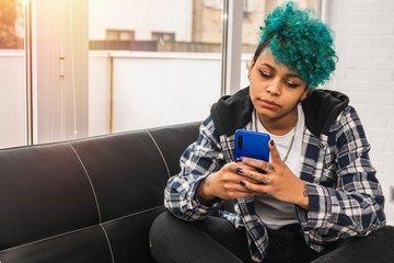 young woman or girl with mobile phone at home or apartment with blue hair afro american curl
