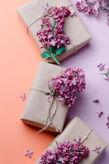 Handmade gift boxes wrapped in kraft brown paper decorated with purple lilac flowers on a pink background. Spring holidays background.