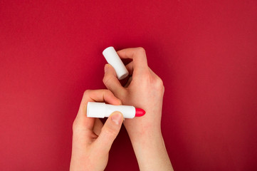 The girl is holding a red lipstick. Tries the product, evaluates.