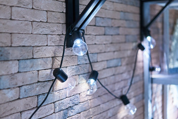 Obraz premium A garland of incandescent bulbs hang in front of a brick wall. Selective focus. Toned
