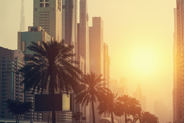 Dubai at sunset. Skyscrapers and high rise city buildings with palms in sunlight, United Arab Emirates, vintage toned