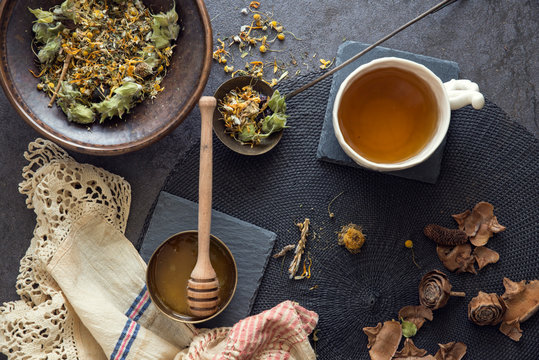Overhead view of a bowl of sleep tea blend tea leaves with chamomile and lemon balm, a Mug of tea and honey on a table
