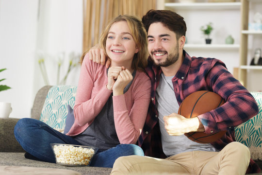 Happy Young Couple Watching Basketball Game On Tv At Home