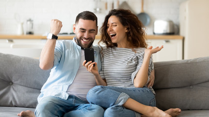 Excited young couple triumph reading news on cell