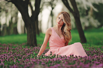 Beautiful blonde young woman in colorful flowers. girl with make-up and hairstyle in pink dress in...