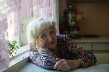 Portrait of an old woman sitting at a table in the house.