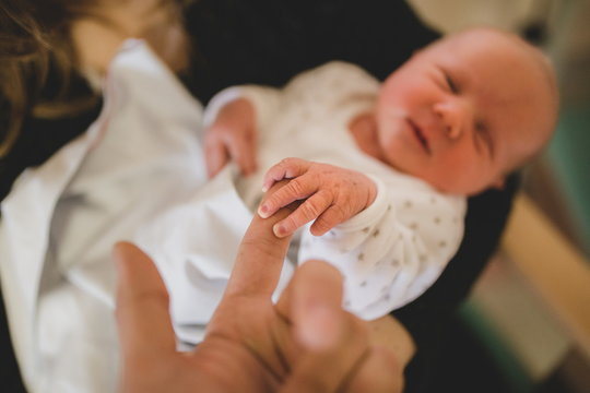 Parent holding in the hands feet of newborn baby. Baby holding man's finger. Newborn baby hand holding mother's finger. Mother care concept. Close-up of baby's hand holding mother's finger. Tenderness