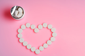 Heart frame made of pills on pink color background, flat lay with space for text.