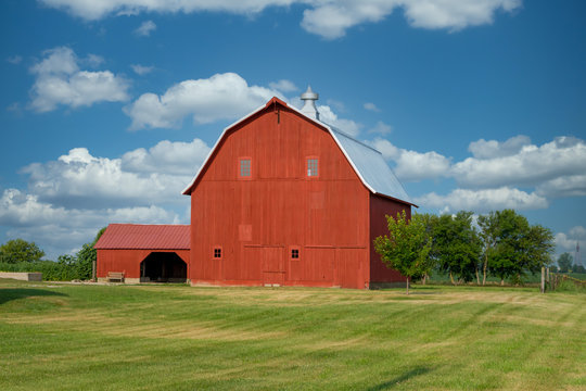 A beautiful, very large, bright red, well kept barn by the side of the road.  The building has a new metal roof, and a side building on the left.