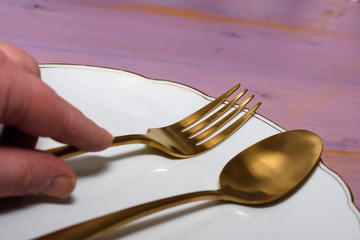 Golden fork  and spoon on white plate held with fingers