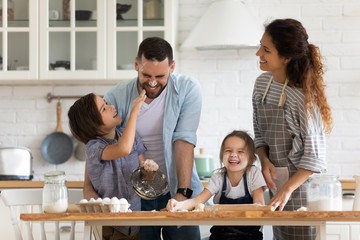 Overjoyed parents with little kids have fun cooking in kitchen