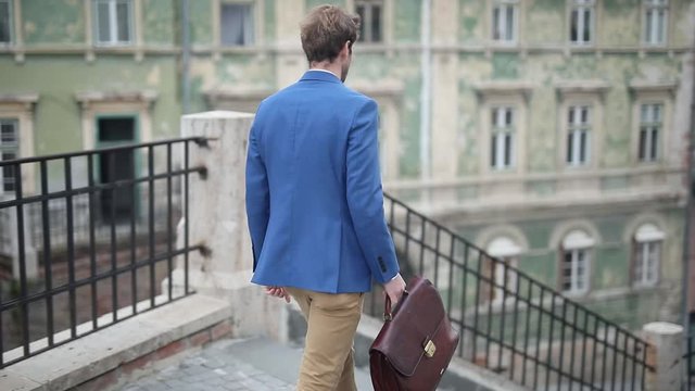  rear view of an atractive businessman wearing navy suit walking down the stairs while holding a briefcase outside in the city