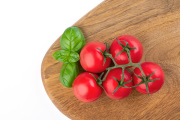 A bunch of tomatoes and a bush of basil on a wooden kitchen board