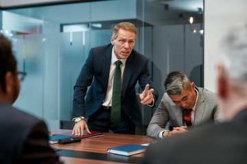 Angry boss. Furious mature businessman in formal wear shouting at his colleagues while having a meeting in the conference room