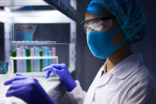 Side View Portrait Of Female Scientist Wearing Face Mask And Protective Gear Working On Research In Laboratory, Copy Space