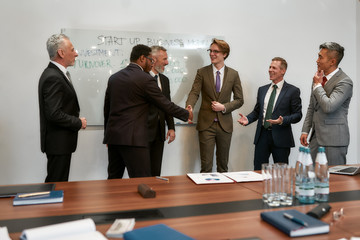 Nice to meet you. Two happy businessmen in classic wear shaking hands while having a meeting with their team in the modern office