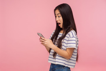 Wow, amazing application! Side view of surprised girl with brunette hair in t-shirt using online...