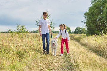 Children walking with white dog in meadow on autumn day