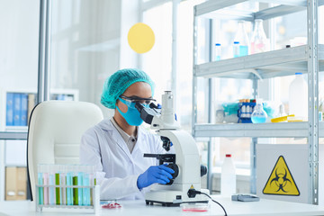 Portrait of female scientist looking in microscope while working on bio hazard research in...