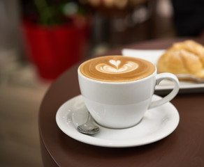 white cup with cappuccino on a brown table
