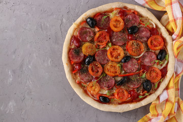 Pizza with sausage, tomatoes, mozzarella and black olives on a gray background, Top view