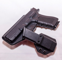 A black pistol in a plastic holster with a loaded magazine holster on a white background