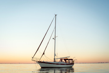 Cutter rigged sailboat with clipper bow and red canvas at sunrise or sunset