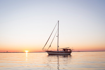 Cutter rigged sailboat with clipper bow and red canvas at sunrise or sunset