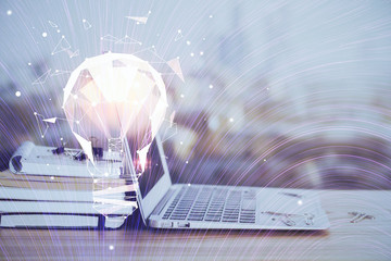 Computer on desktop in office with bulb icon hologram. Multi exposure. Concept of idea.