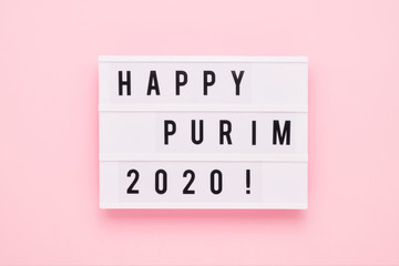Purim celebration concept. "Happy Purim" written in light box on pink background. Top view, copy space.