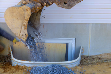 Bucket moving gravel in the windows well on basement construction from window
