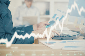 Double exposure of graph with man typing on computer in office on background. Concept of hard work....