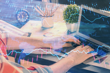 Double exposure of stock graph with businessman typing on computer in office on background. Concept of hard work.