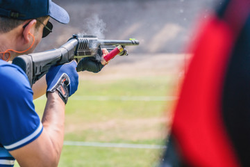 selective focus of man holding and fire shortgun in shooting range of gun shooting competition