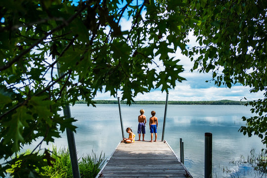 Rear view of three children in swimwear on a wooden jetty fishing on a summer day
