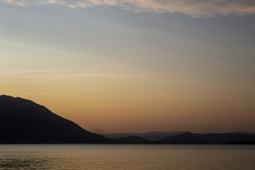 Fototapeta premium Sunset with orange tones on the sky reflecting in the sea with mountains at the horizon seen from Florianópolis