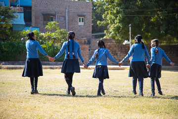 Indian asian happy school girls holding hands and walking playing in a garden wearing school uniform.