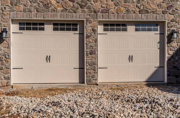 Two single car classic insulated steel panel garage door framed with  architectural stone to add accent, with transom light windows divided by muntins grills on a new American home under construction - obrazy, fototapety, plakaty