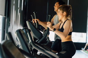 Fototapeta na wymiar Attractive Asian fitness woman using elliptical trainer at the gym with copy space. Healthy and weight loss lifestyle