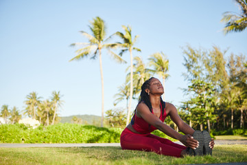 Fit woman sitting on ground, keeping legs straight and together, holding her feet and bending upper...