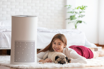 Woman playing with Dog Pug Breed and Air purifier in cozy white bed room for filter and cleaning...