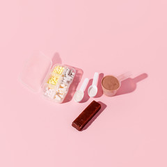 Fitness and healthy lifestyle Supplements - pills tablets, energetic bars, protein powder with shadow on pink background, copy space, concept of nutrition fit bodycare diet, modern health food