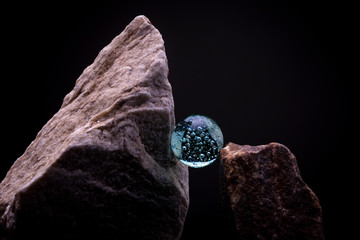 Vibrant blue glass marble between reflecting textured surface of a white stone and brown mining rock. Abstract concept.