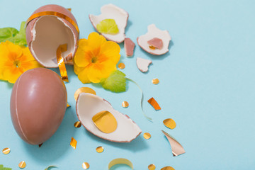 Easter chocolate egg with golden confetti and spring flowers on blue background