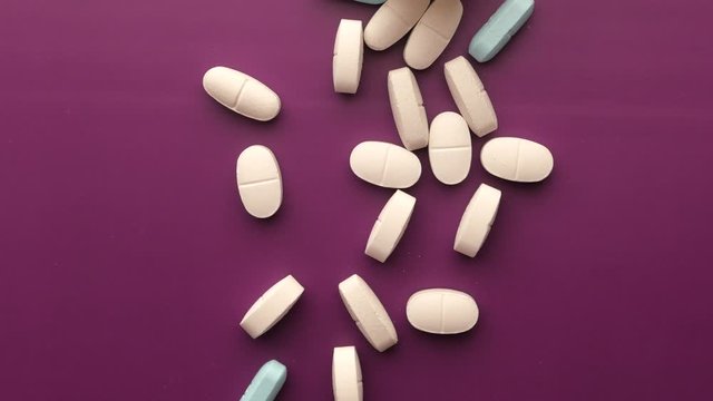 Close up of pills spilling from container on purple background 