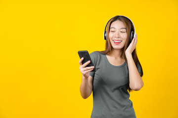 Happiness Asian smiling young woman wearing technology wireless headphones for listening the music via smart mobile phone on isolated yellow color background, Lifestyle and leisure with hobby concept