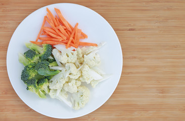 Obraz na płótnie Canvas Cauliflower, broccoli and carrots on a plate against wooden background with copy space.